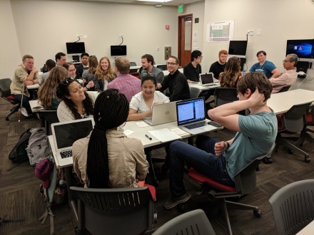Students sitting at tables and speaking to each other.