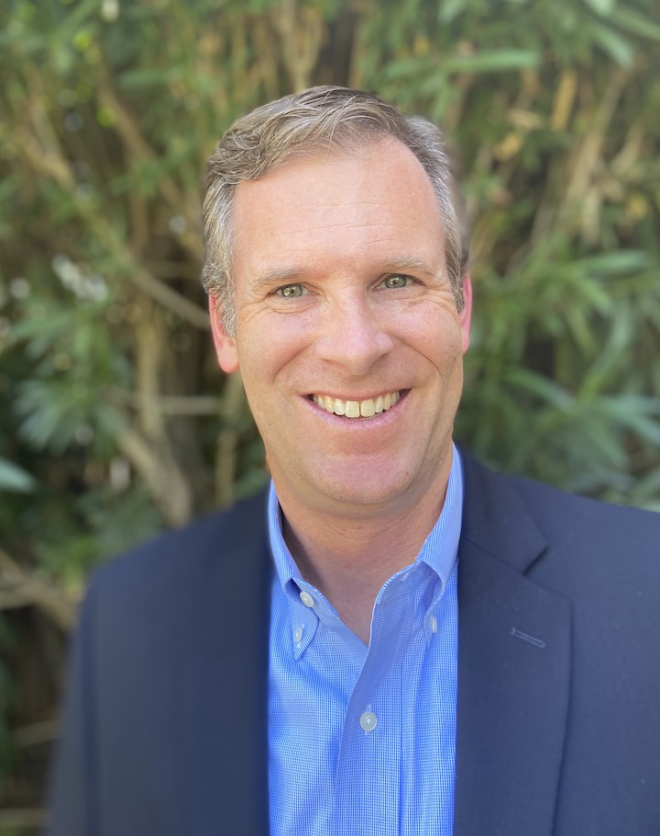 Sean Keagan has grey hair and blue eyes. He is smiling and wearing a blue shirt with a navy blazer