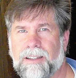 Larry has blue eyes and grey hair. He has a big grey beard and is smiling at the camera