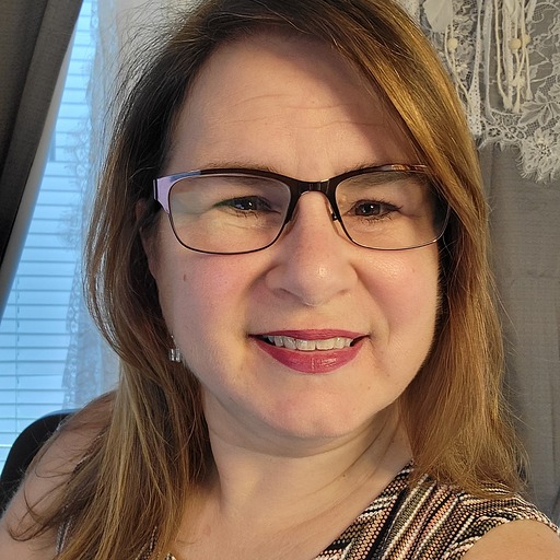 Mindy Kolin has medium brown, shoulder-length hair. She is wearing pink lipstick and has glasses. She is smiling at the camera