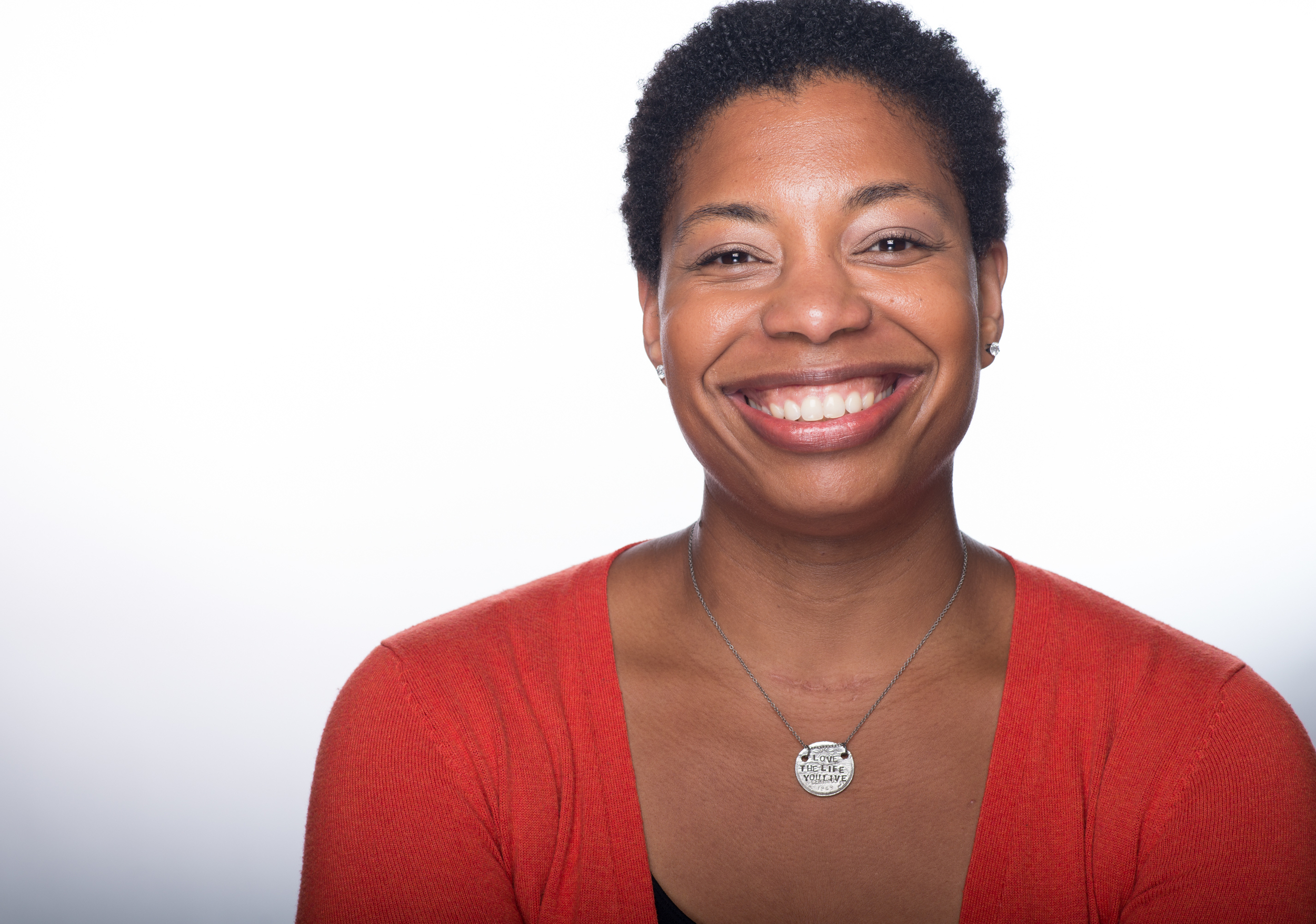Regine has short black hair and brown eyes. She has a big smile and is wearing a red shirt with a silver necklace.