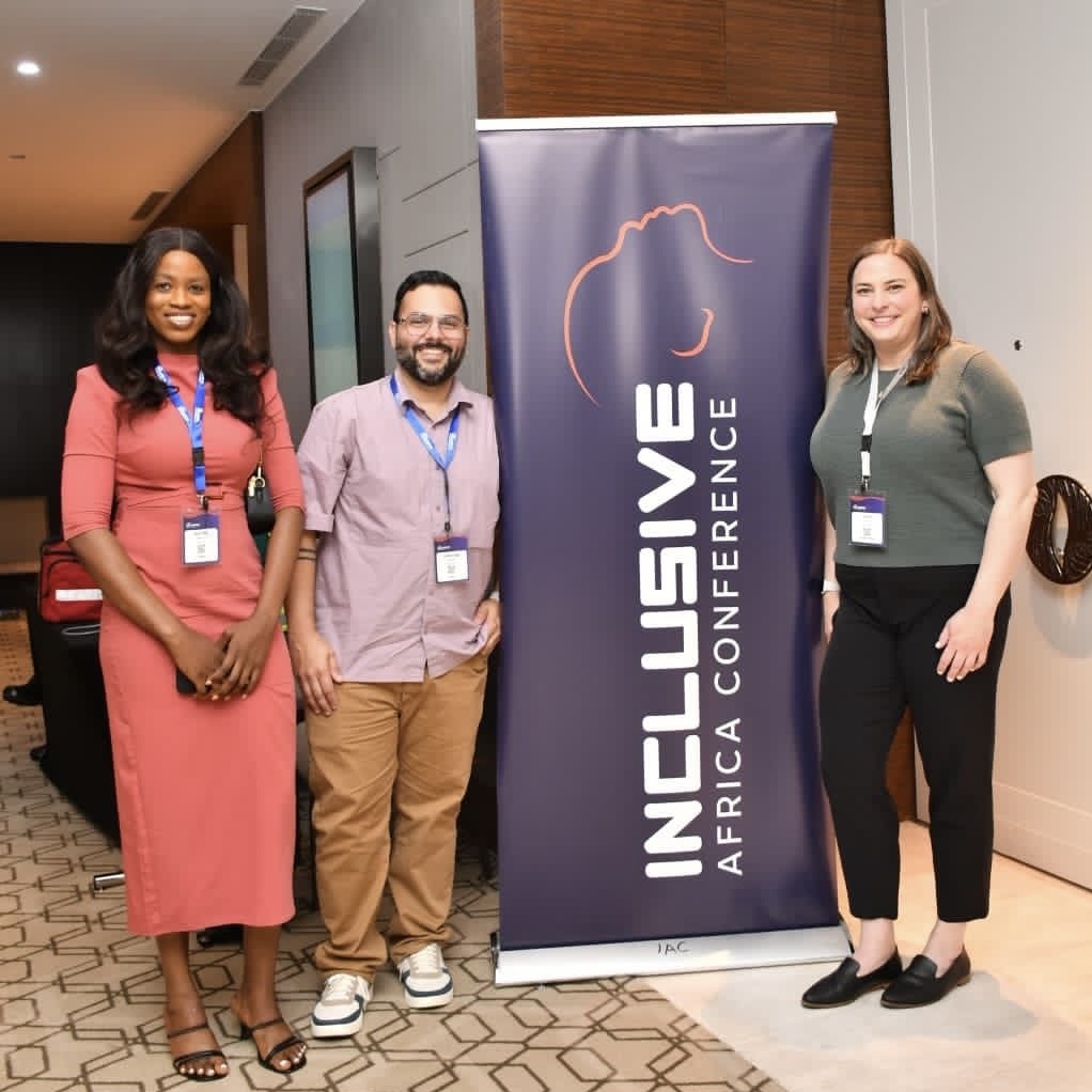 Renike, Rolando, and Kate posing next to an Inclusive Africa Conference banner.