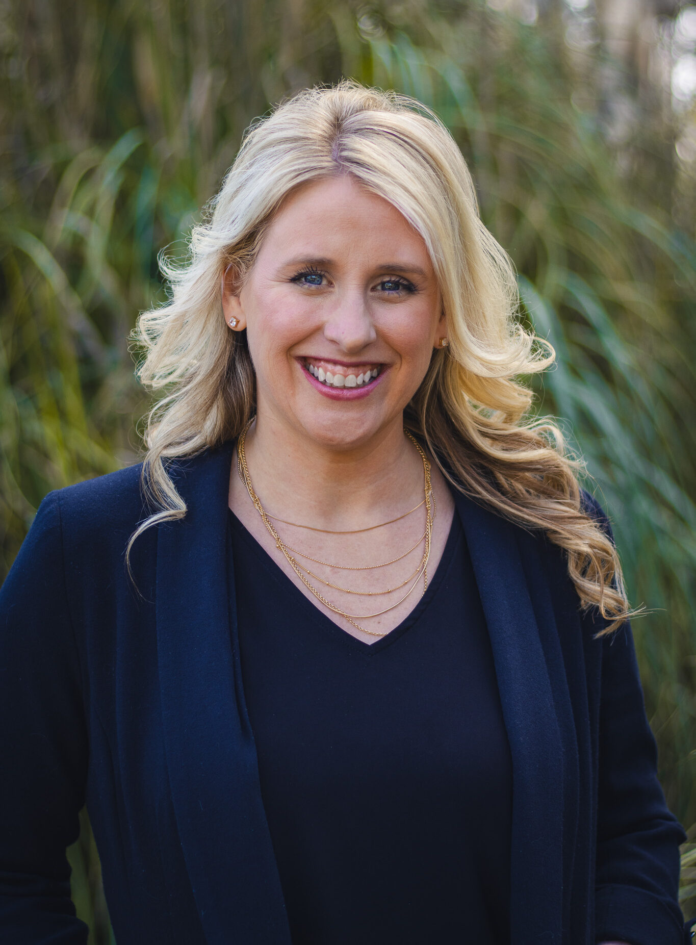 Headshot of Leslie smiling, blonde hair, fair skin, blue eyes, wearing dark shirt and jacket.