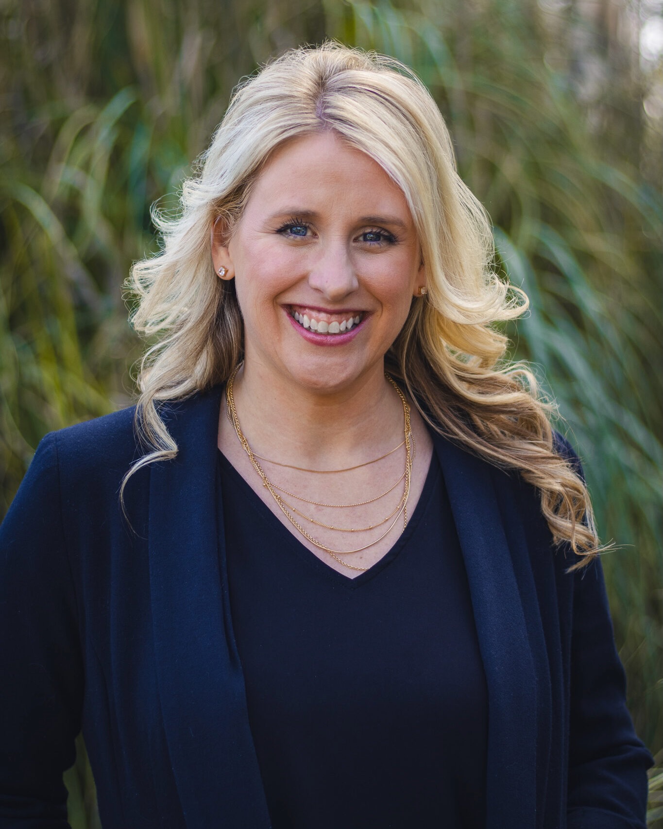 Headshot of Leslie smiling, blonde hair, fair skin, blue eyes, wearing dark shirt and jacket.