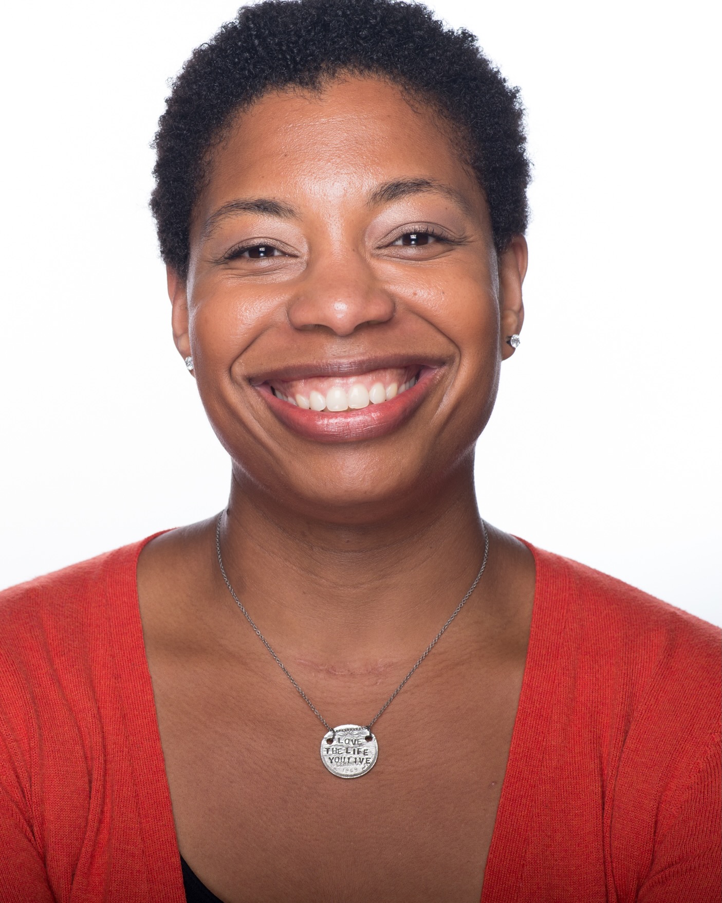 Regine has short black hair and brown eyes. She has a big smile and is wearing a red shirt with a silver necklace.