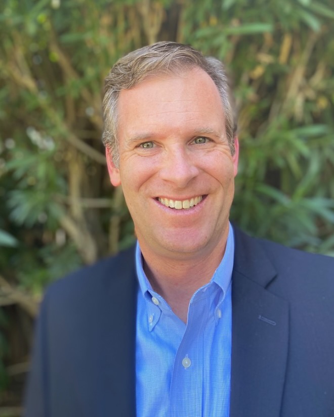 Sean Keagan has grey hair and blue eyes. He is smiling and wearing a blue shirt with a navy blazer