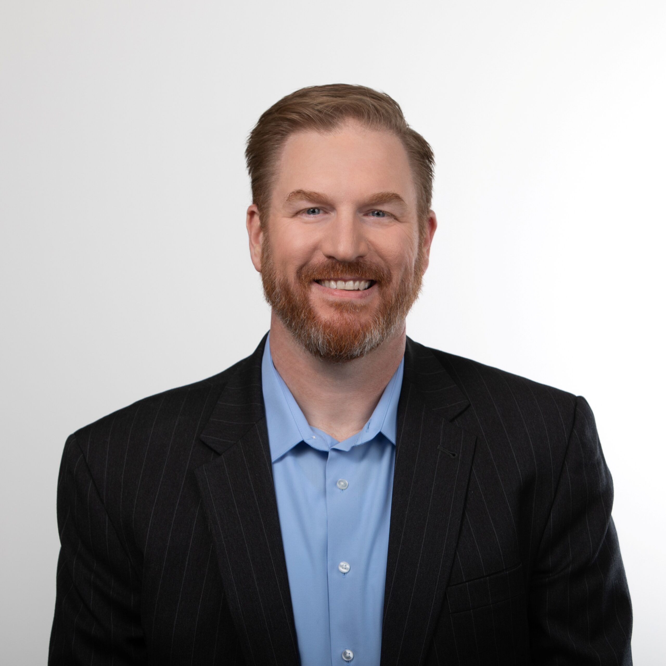 Steve Ewell, a man person with light skin and reddish-brown hair, in a dark suit and light blue shirt, smiling against a white background.